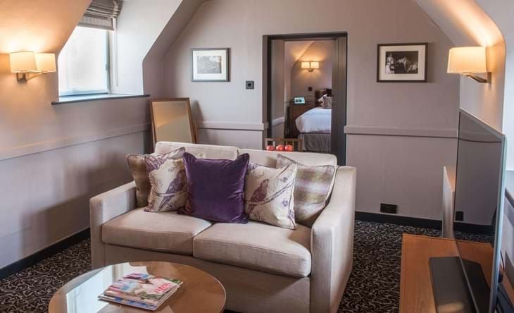 Elegant historic suite with rich wooden furnishings, plush king bed, classic British décor, and luxurious period details at renowned Cotswolds hotel