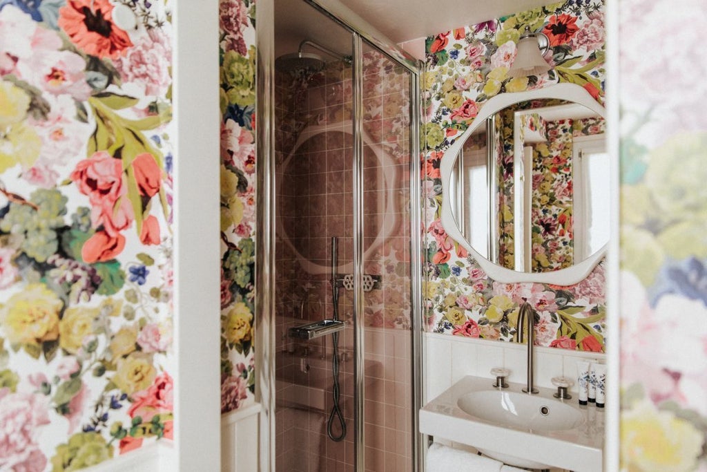 Elegant Parisian boutique hotel room with plush white bedding, soft pastel walls, ornate vintage chandelier, and large arched window overlooking charming street