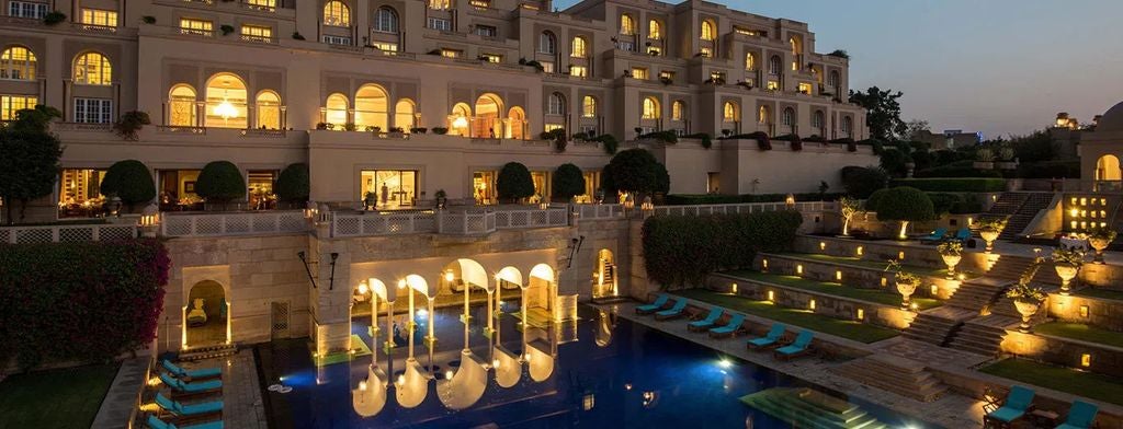 Opulent sandstone hotel with Moorish architecture, grand archways and domed towers overlooking manicured gardens near the Taj Mahal