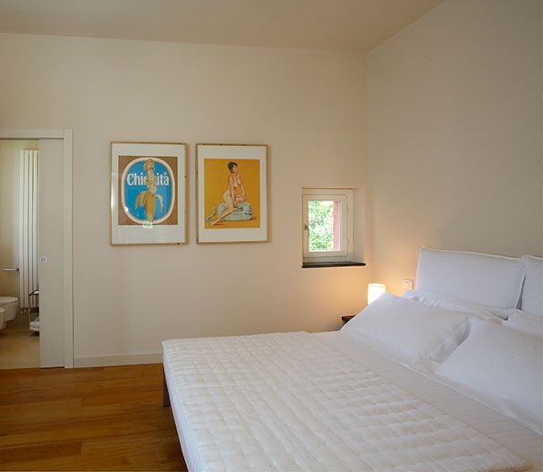 Elegant Italian villa bedroom with soft rosemary tones, plush white linens, antique wooden furniture, and a panoramic view of lush Mediterranean landscape.