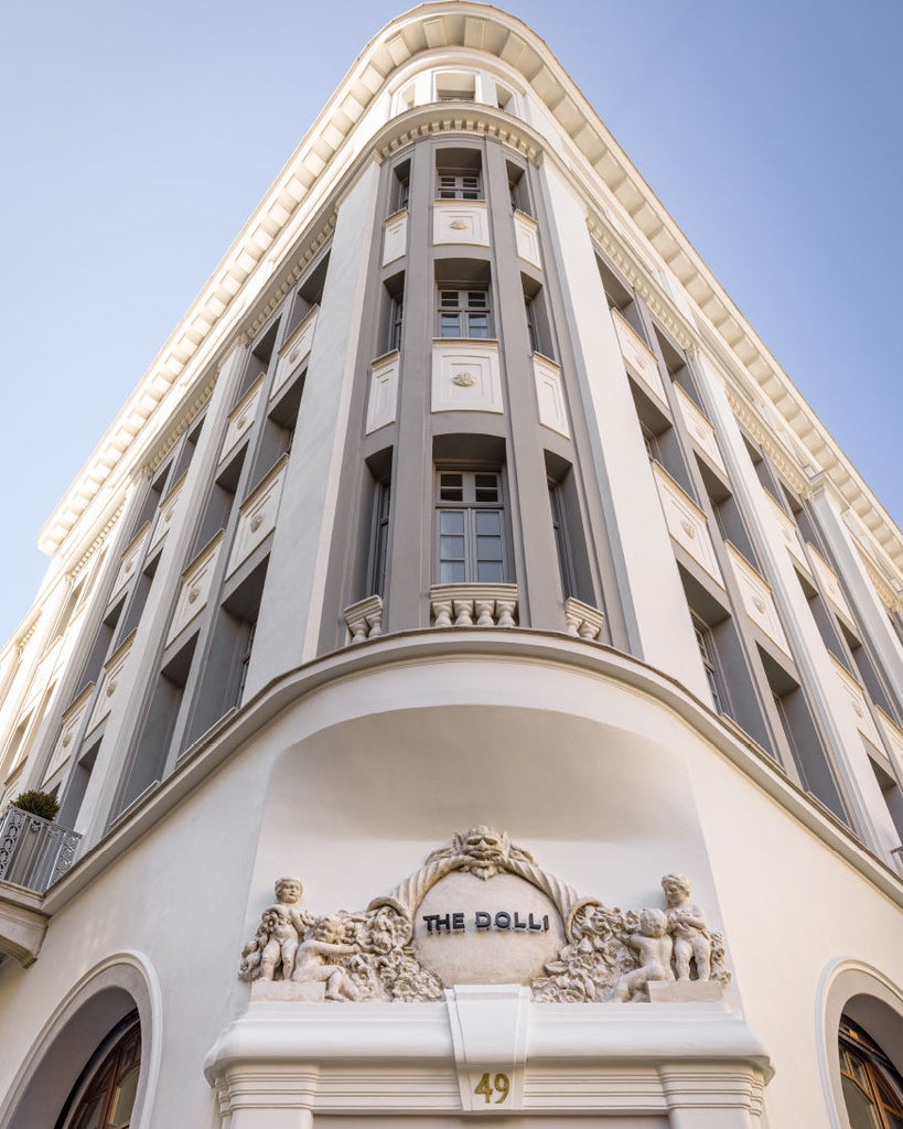 Luxurious white Mediterranean hotel building with curved balconies, overlooking the Aegean Sea against a dramatic cliff backdrop