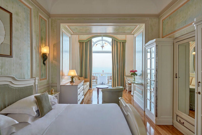 Elegant deluxe room with French doors opening to private balcony overlooking Mediterranean Sea, classic Italian furnishings, chandelier