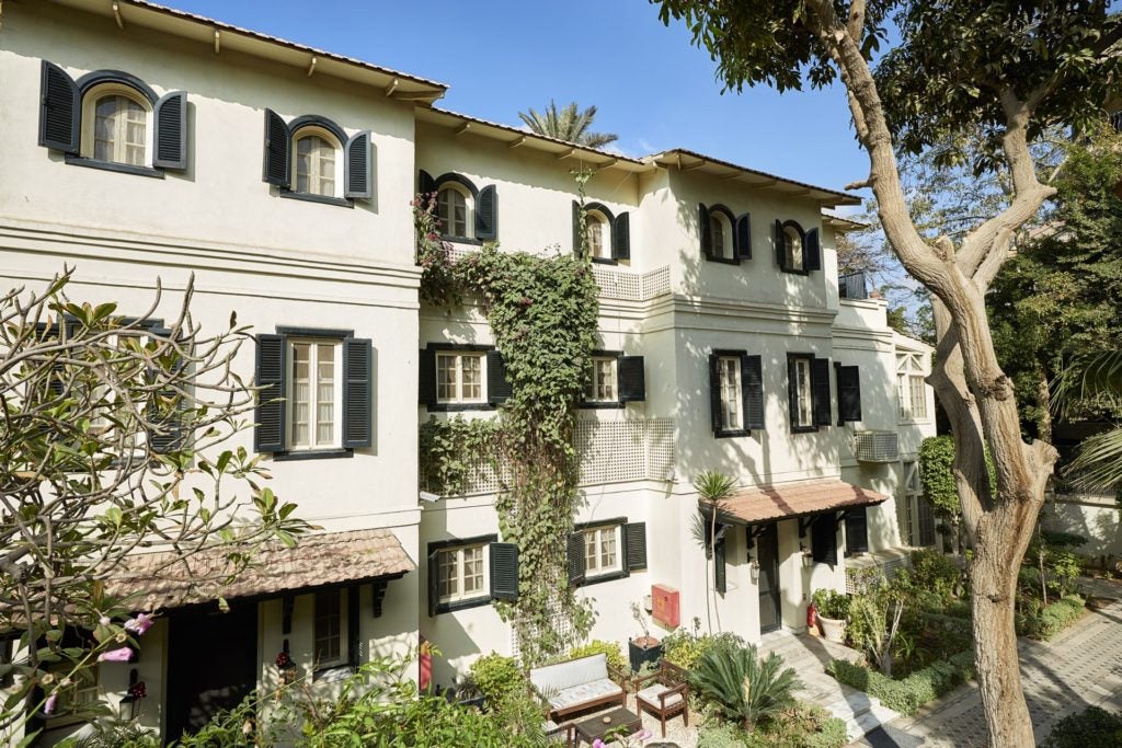 A sun-drenched luxury boutique hotel with white colonial facade, palm trees, and manicured gardens in Cairo's historic Maadi district