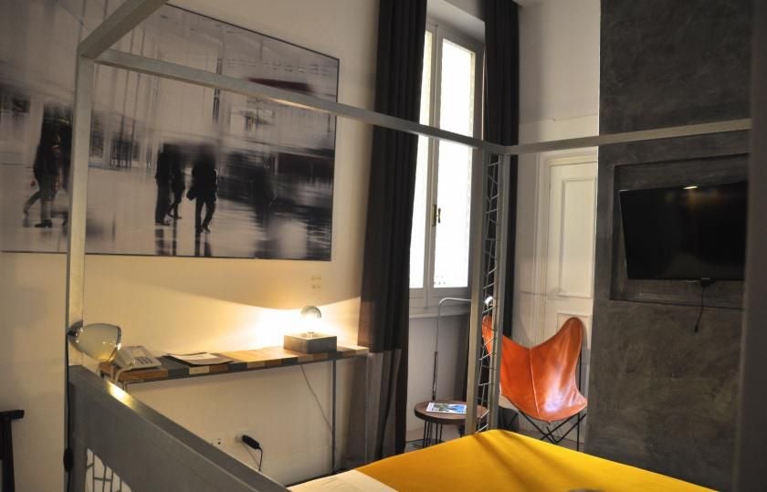 Elegant modern hotel room with soft neutral tones, plush white bedding, minimalist decor, and large windows overlooking historic Italian architecture in Rome