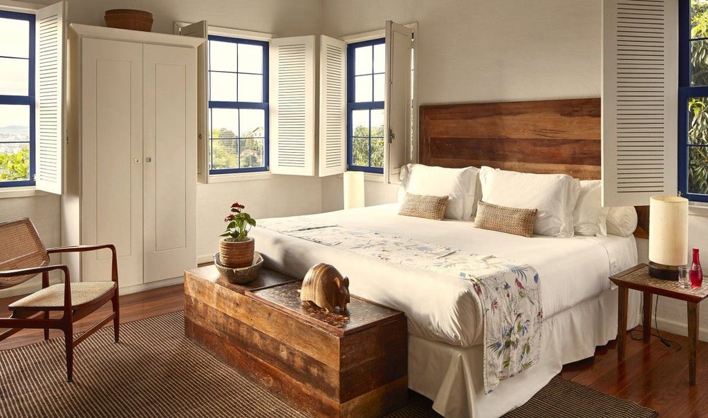 Elegant superior room at Santa Teresa Hotel, Rio de Janeiro, featuring sophisticated Brazilian decor, plush bedding, and warm wooden accents with soft lighting