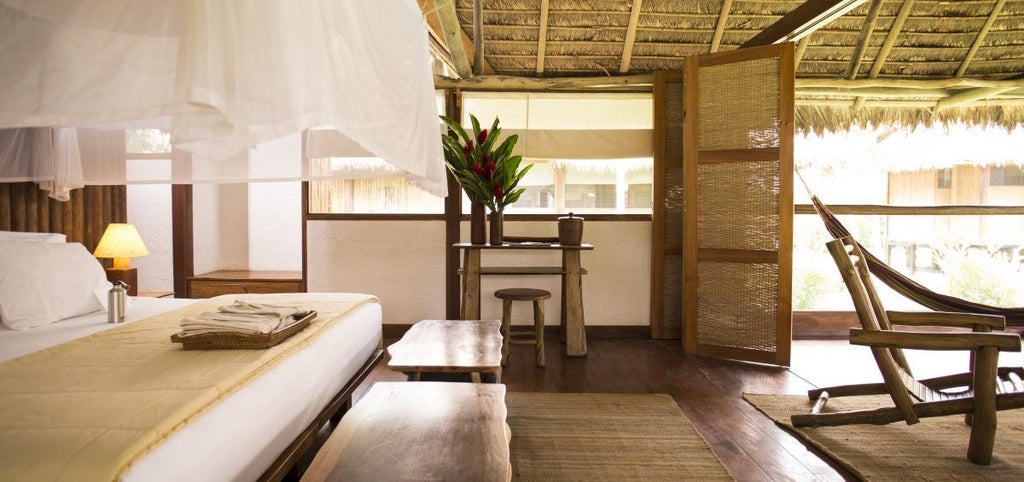 Elevated wooden cabin with thatched palm roof nestled in lush Amazon rainforest, featuring private terrace and luxury amenities