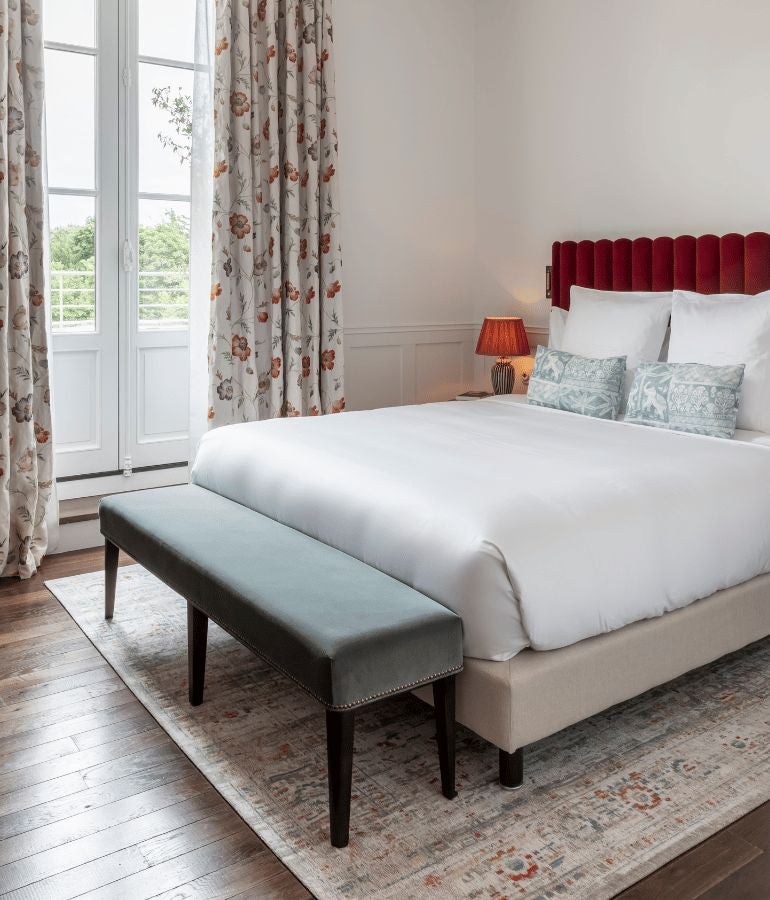 Elegant French hotel room with soft neutral tones, plush bedding, ornate wooden furnishings, and refined architectural details reflecting sophisticated coastal hospitality