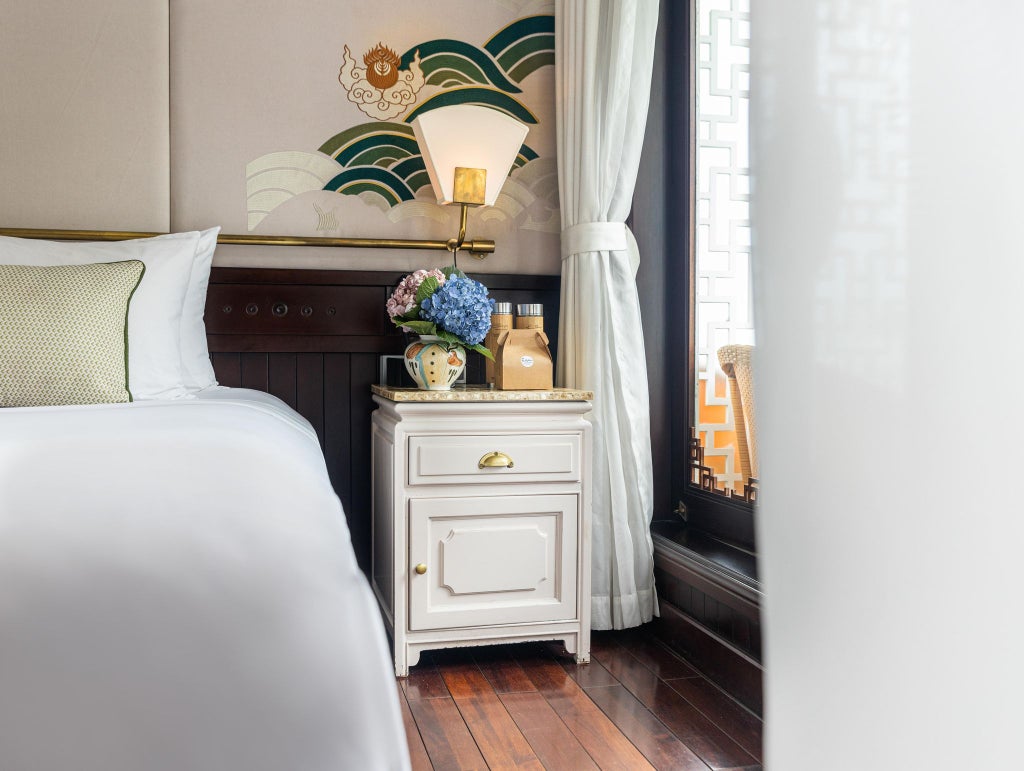 Elegant wood-paneled deluxe cabin aboard Bhaya Cruises, featuring plush bedding, traditional Vietnamese design, and panoramic windows overlooking halong bay.