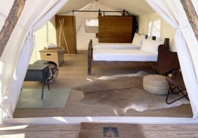 Luxurious safari-style canvas tent suite with king bed, wooden furnishings, and large windows overlooking scenic Zion National Park landscape at Under Canvas resort