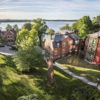 Luxurious waterfront hotel with sleek Scandinavian design, glass façade reflecting blue fjord waters and surrounding pine forest landscape in Sweden