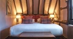 Elegant superior room at The Lygon Arms, featuring plush bedding, classic British decor, warm wood furnishings, and soft neutral color palette in historic Cotswolds setting