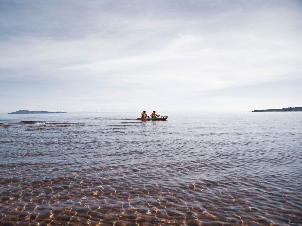 Modern luxury lodge with stone and glass architecture perched on Lake Titicaca's shore at sunset, featuring panoramic waterfront views