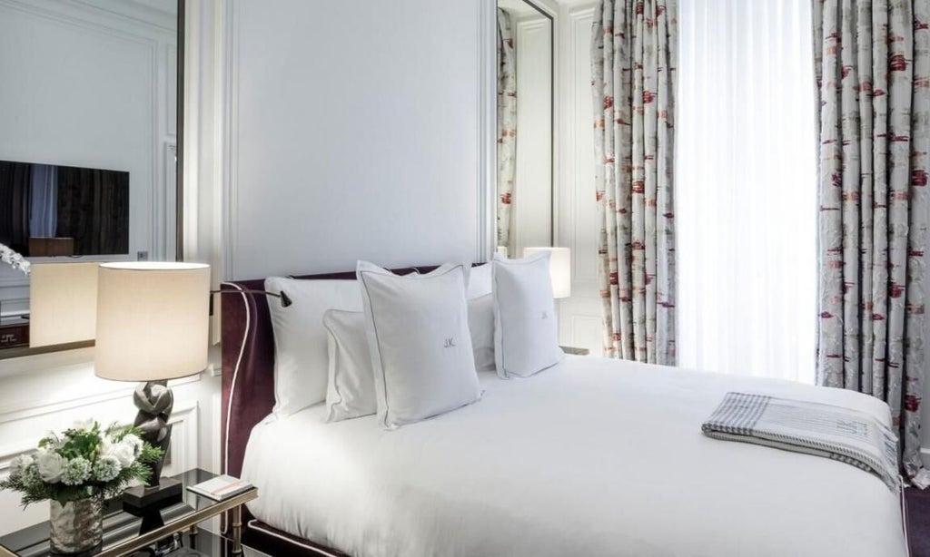 Elegant Parisian hotel room with plush white bedding, ornate gold-framed mirror, soft neutral tones, and chic designer furnishings in luxurious boutique setting