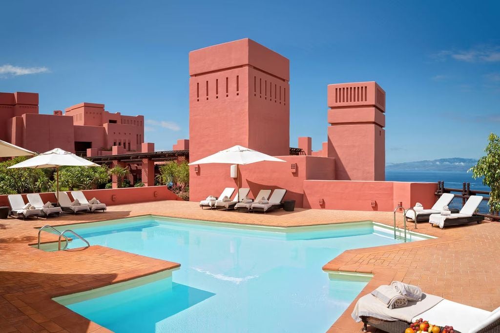 Five-star resort with terracotta buildings cascading down a lush hillside, featuring multiple pools and ocean views in Tenerife.