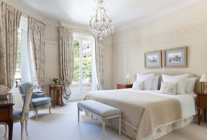 Elegant deluxe hotel room with ornate gold furnishings, French balcony doors, crystal chandelier and plush king bed with luxe linens