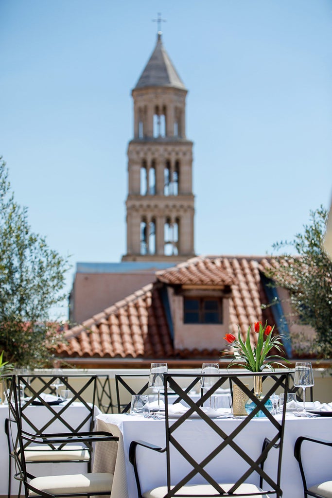 Contemporary beachfront hotel with white stone facade, private balconies overlooking the Adriatic Sea, surrounded by swaying palms and landscaped gardens