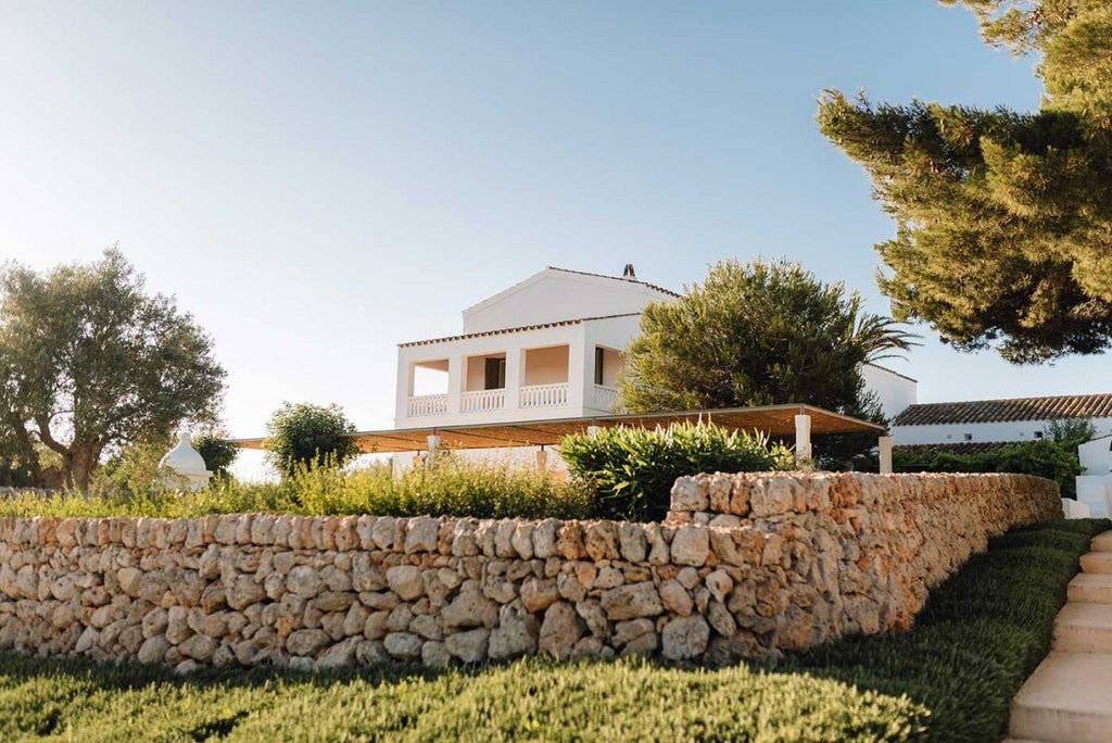 Elegant stone finca-style hotel nestled in Menorca's countryside, featuring rustic white buildings, lavender fields, and a serene Mediterranean landscape