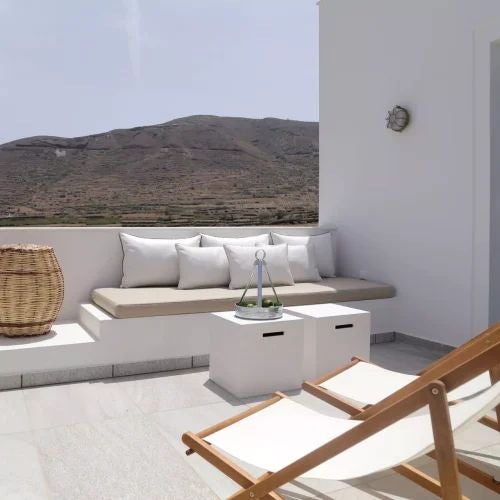 Luxurious Vinsanto Villa bedroom with white stone walls, elegant wooden furniture, and panoramic view of Grecian landscape through arched window