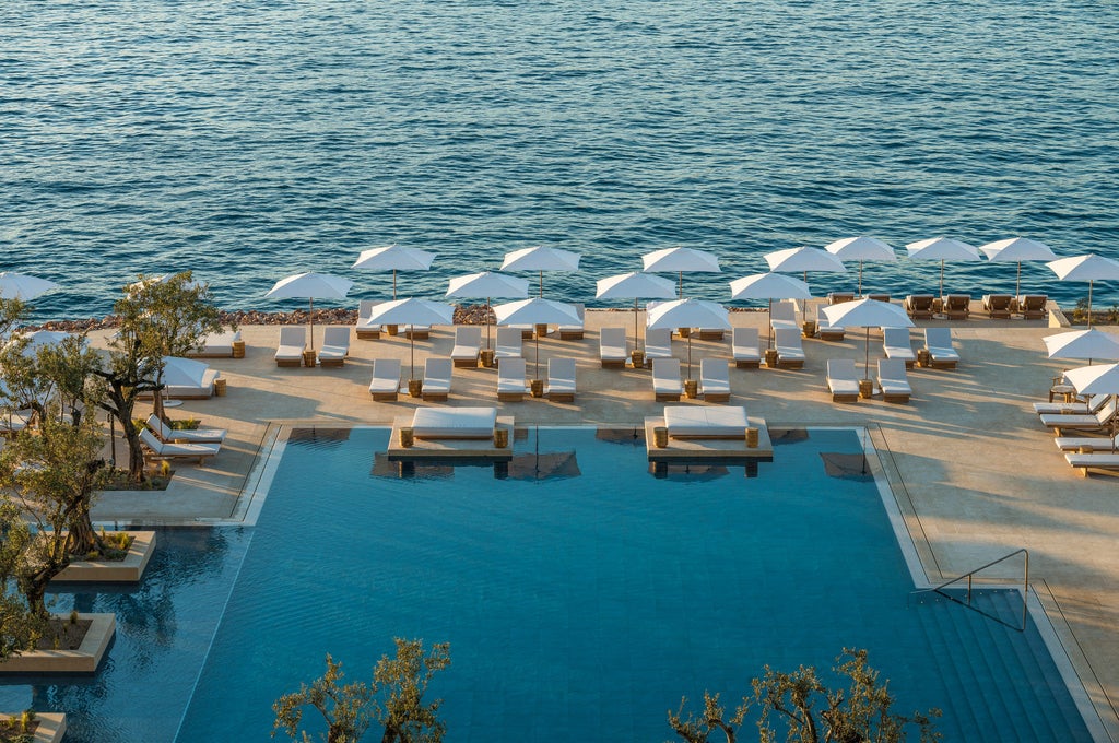 Elegant beachfront resort with infinity pools overlooking the Aegean Sea, white cabanas and private terraces bordered by palm trees