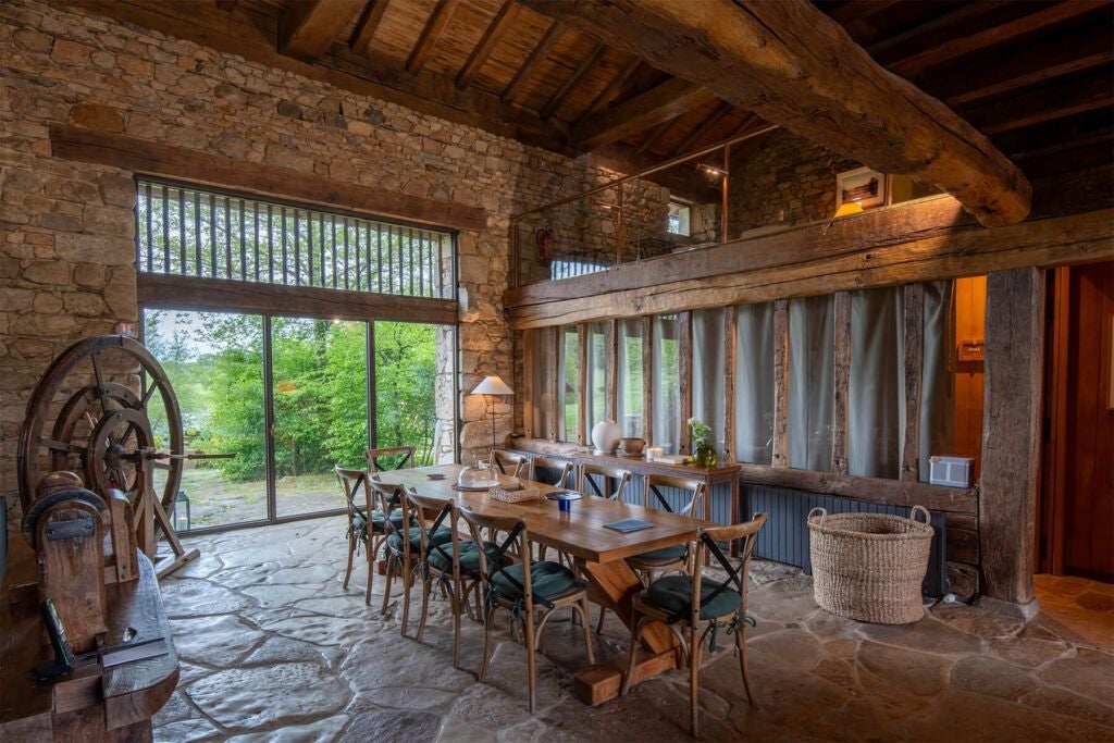 Luxurious French cottage bedroom with rustic wooden floors, expansive windows, elegant four-poster bed, and soft natural light in Domaine des Etangs