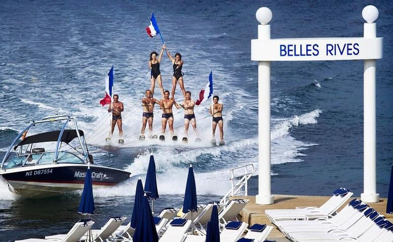 Elegant 1930s art deco hotel Belles Rives with white facade overlooking Mediterranean Sea, featuring palm trees and private beach pier