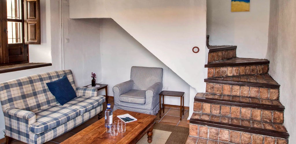 Rustic Spanish luxury suite with white-washed walls, exposed wooden beams, elegant antique furnishings, and soft natural light in Cortijo del Marqués