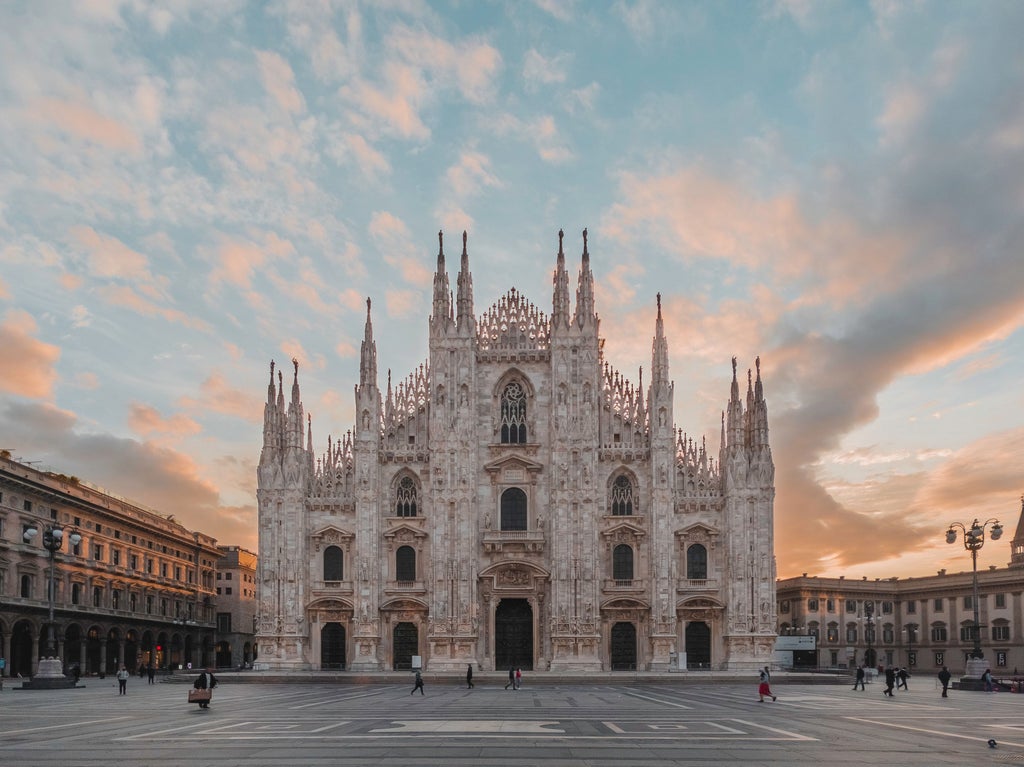 Historic Milan Cathedral's ornate Gothic spires and marble facade rise against a blue sky, with elegant stone statues adorning its exterior