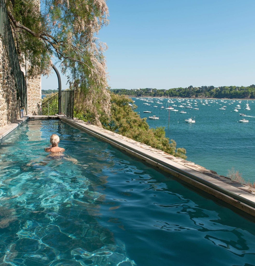 Luxurious coastal hotel with elegant blue and white facade, perched on rocky cliff overlooking azure waters of Brittany shoreline