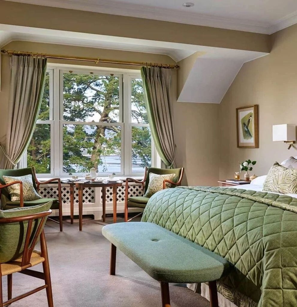 Elegant hotel room with king bed, classic furnishings, and floor-to-ceiling windows offering panoramic views of the Irish countryside