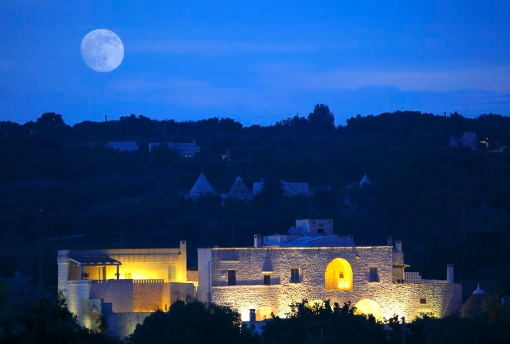 Rustic stone-walled luxury hotel nestled in Puglia's countryside, featuring elegant stone archways, warm terracotta tiles, and lush Mediterranean vegetation