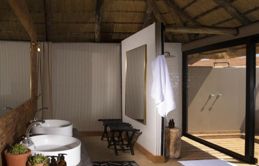 Light-filled luxury twin bedroom in desert lodge featuring canvas walls, wooden floors, and panoramic windows overlooking Namibian dunes