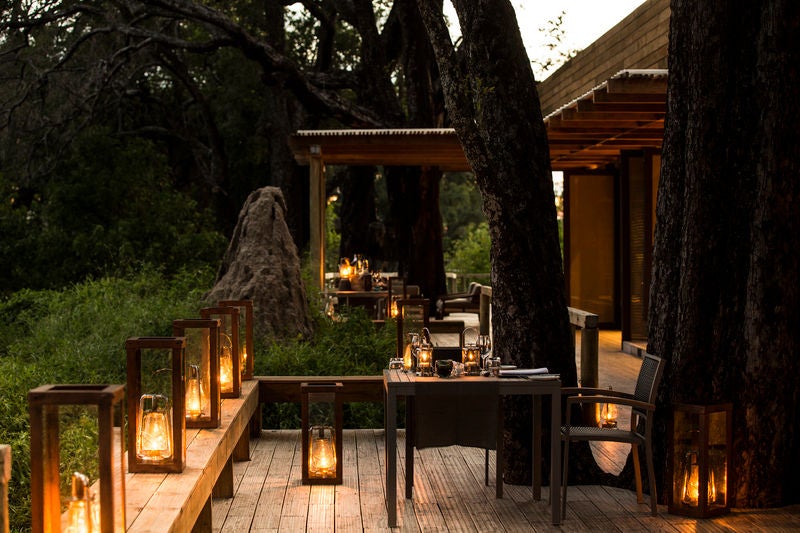 Luxurious safari camp tent with private deck overlooking flooded Okavango Delta plains, surrounded by lush palm trees at sunset