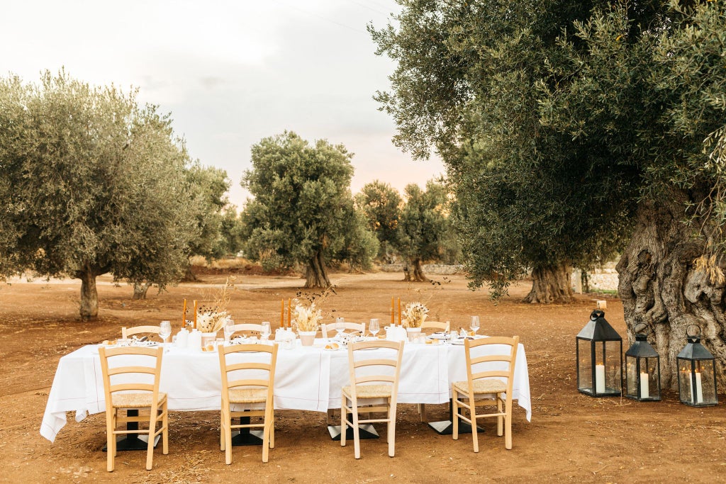 Rustic luxe stone villa nestled in golden Puglia countryside, with stone-walled terrace overlooking vibrant olive groves and azure Mediterranean landscape