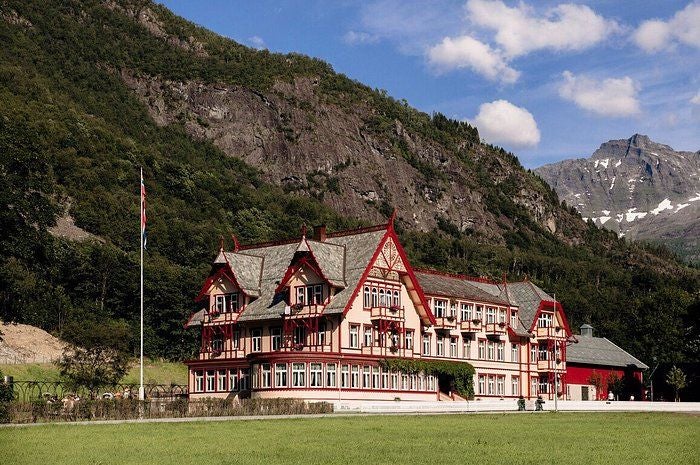 Historic Norwegian luxury hotel with grand white facade, ornate architecture, and gabled roofs nestled against dramatic mountain peaks