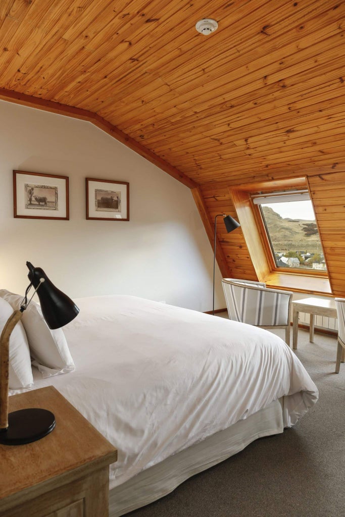 Elegant standard room at Los Cerros Boutique Hotel, featuring plush white bedding, wooden floors, and warm mountain-view lighting in Argentina.