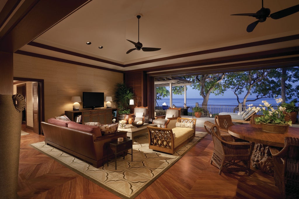 Oceanfront luxury resort with infinity pool merging into Pacific horizon, surrounded by swaying palms and black lava rock landscapes