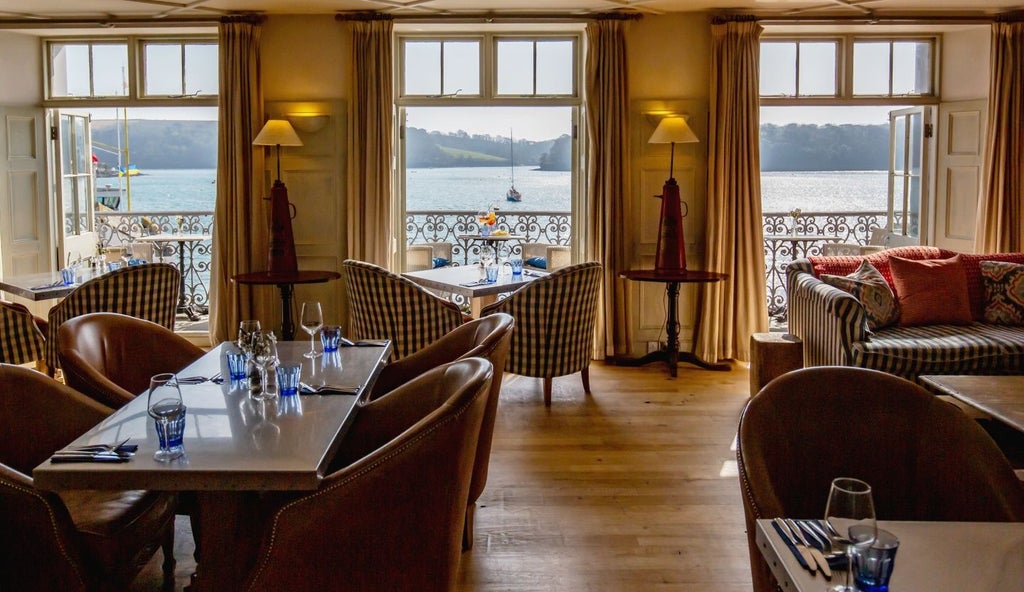 Luxurious coastal hotel with white exterior, panoramic sea views, nestled in picturesque Cornish landscape with pristine blue waters and rocky shoreline