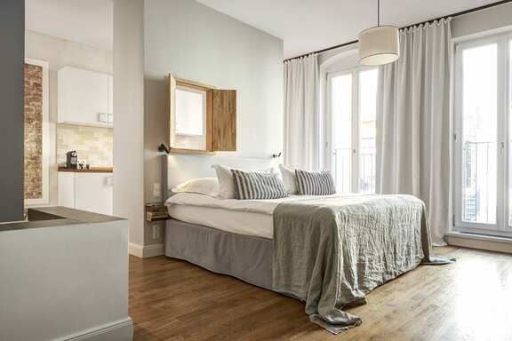 Modern, spacious German hotel room with minimalist design, plush white bedding, sleek wooden furnishings, and large window overlooking urban landscape at Gorki Apartments