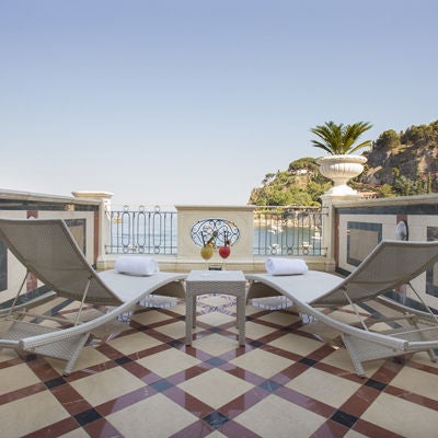 Elegant hotel room with sea-view balcony, featuring cream marble floors, ornate furnishings, and a king-size bed with golden accents