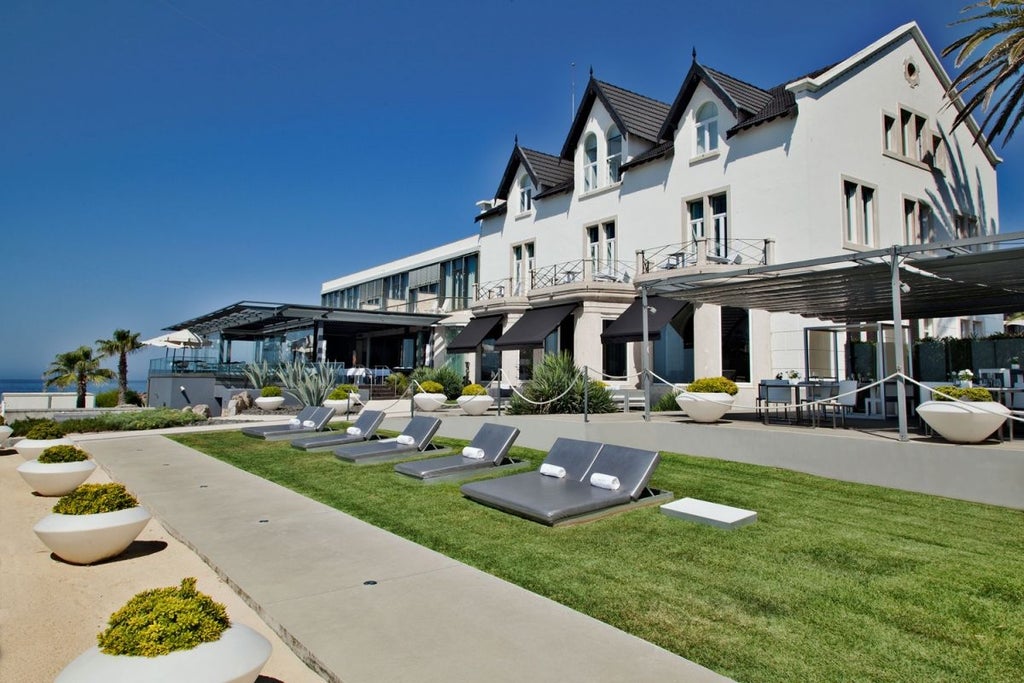 Luxurious whitewashed coastal resort with blue-trimmed windows overlooking dramatic rocky shoreline and turquoise Atlantic waters in scenic Portugal