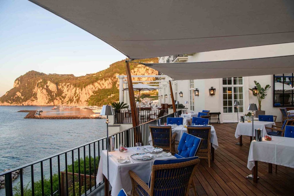 Elegant Mediterranean terrace of JK Place Capri hotel overlooking bright blue waters, with white columns and plush outdoor seating