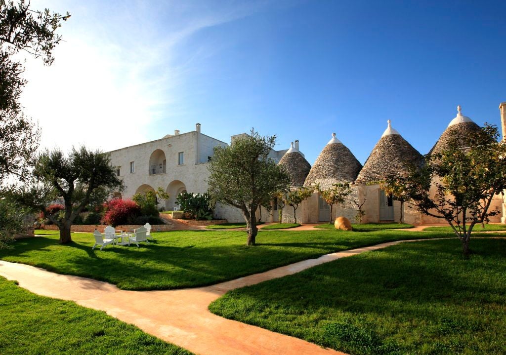 Rustic stone luxury hotel nestled in Puglian countryside, with sun-drenched stone walls, terracotta roof, and lush olive grove surroundings in southern Italy