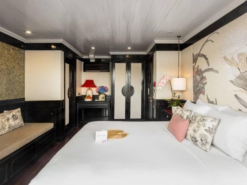 Luxurious Long Quan Suite aboard Bhaya Cruises with elegant wooden furnishings, panoramic windows overlooking scenic Halong Bay waters in Vietnam