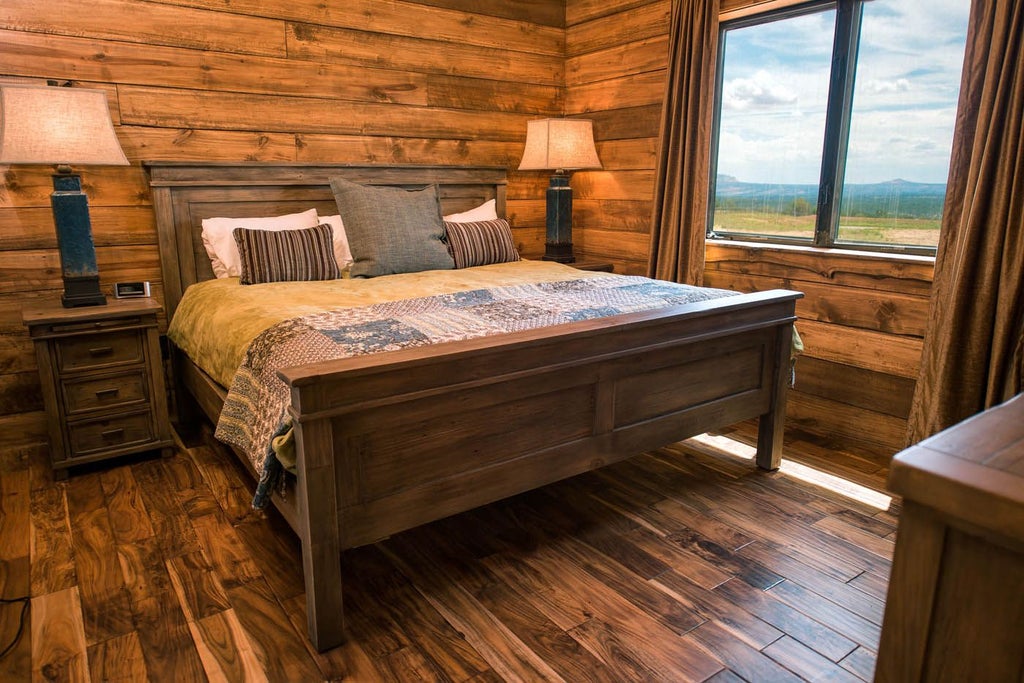 Rustic lodge room with wooden furnishings, plush bedding, large windows overlooking scenic mountain landscape at scenic Mountain Ranch in southwestern United States