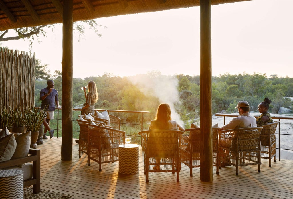 Luxurious safari lodge with thatched-roof suites overlooking a tranquil river, surrounded by African bushveld at golden hour