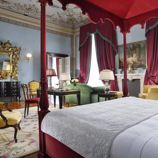 Opulent Imperial Suite with ornate gold-framed mirrors, crystal chandelier, antique furniture, and luxurious red silk damask wallpaper.