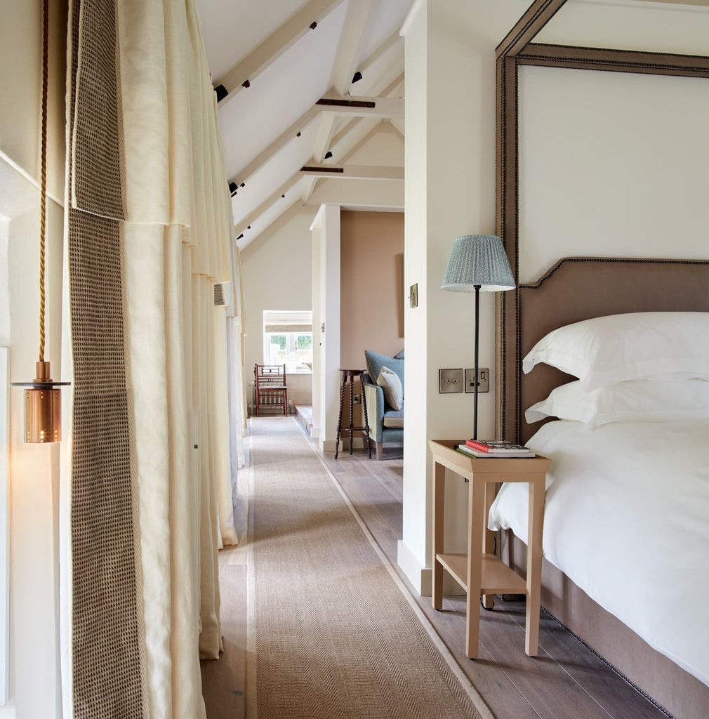 Elegant boutique hotel room with plush white bedding, soft neutral tones, antique wooden furniture, and delicate floral accents in a luxurious UK countryside setting