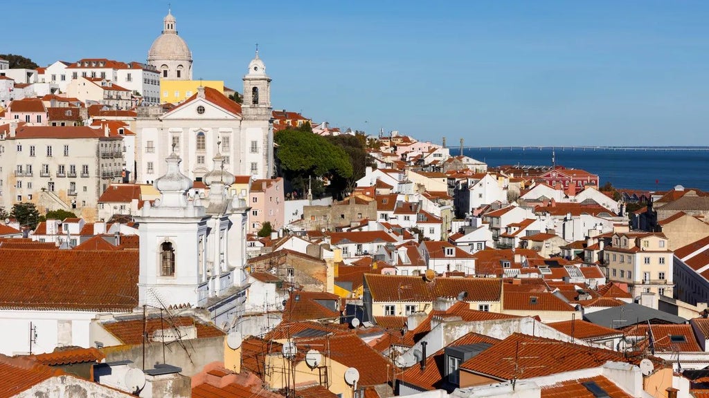 Sunset over Lisbon's historic Alfama district, showcasing a luxurious boutique hotel terrace with panoramic city views and traditional Portuguese tile details