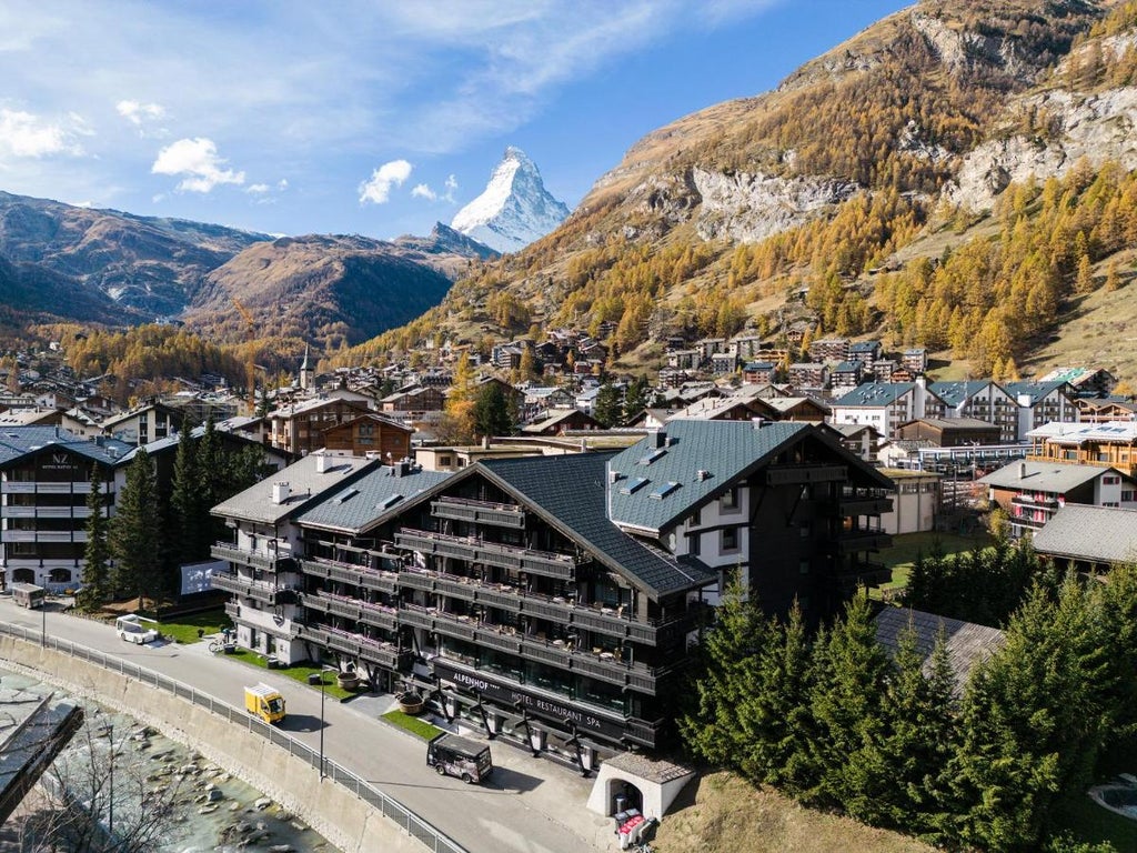 Luxury alpine hotel with wooden balconies and white facade nestled against snow-capped Swiss mountains in a pristine valley setting