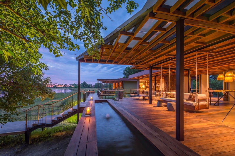 Elevated luxury safari lodge with thatched roof and wooden deck overlooking pristine wetlands during golden evening light in Botswana